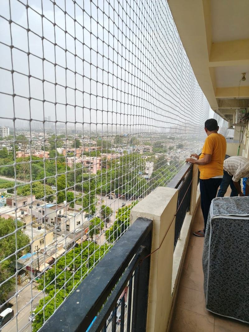 Technician installing an anti bird net along a long balcony corridor