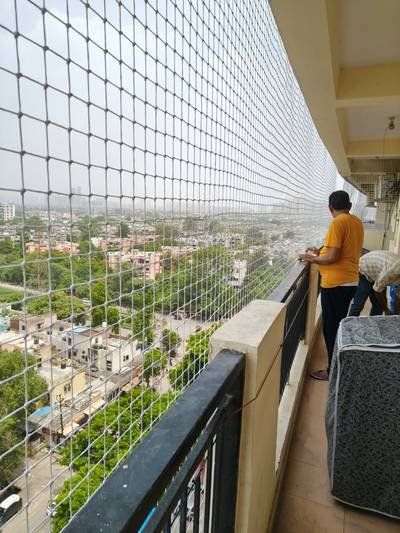 Technician installing anti bird net along a long balcony corridor