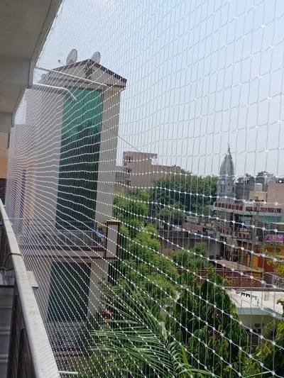 Balcony bird net with a high-rise tower and greenery beyond